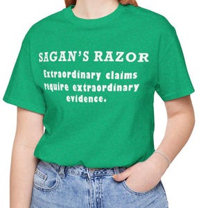以下が含まれることがあります： 白い文字で「SAGAN'S RAZOR Extraordinary claims require extraordinary evidence.」と書かれた緑色のTシャツです。