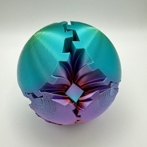 May include: A 3D printed sphere with a geometric design. The sphere is made of a plastic material and is painted in a gradient of blue, purple, and pink.