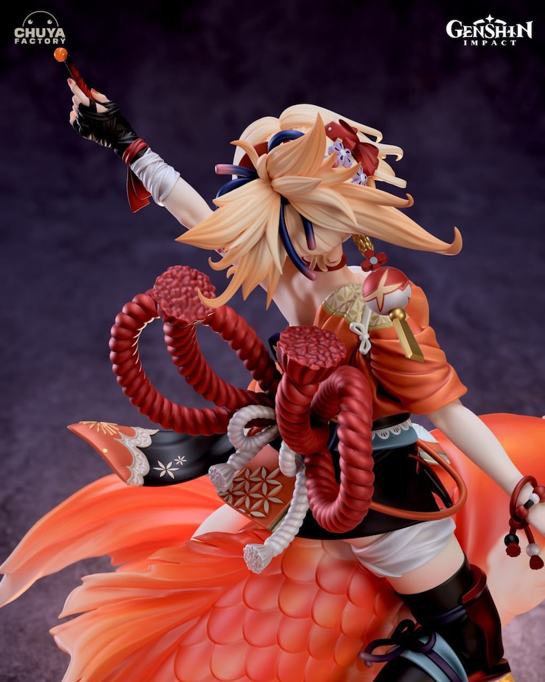 May include: A detailed figurine of a character from the video game Genshin Impact. The character is a young woman with long, flowing blonde hair, wearing a red and orange outfit with a fishtail. She is holding a red and white staff in her right hand. The figurine is made of high-quality materials and is very detailed.
