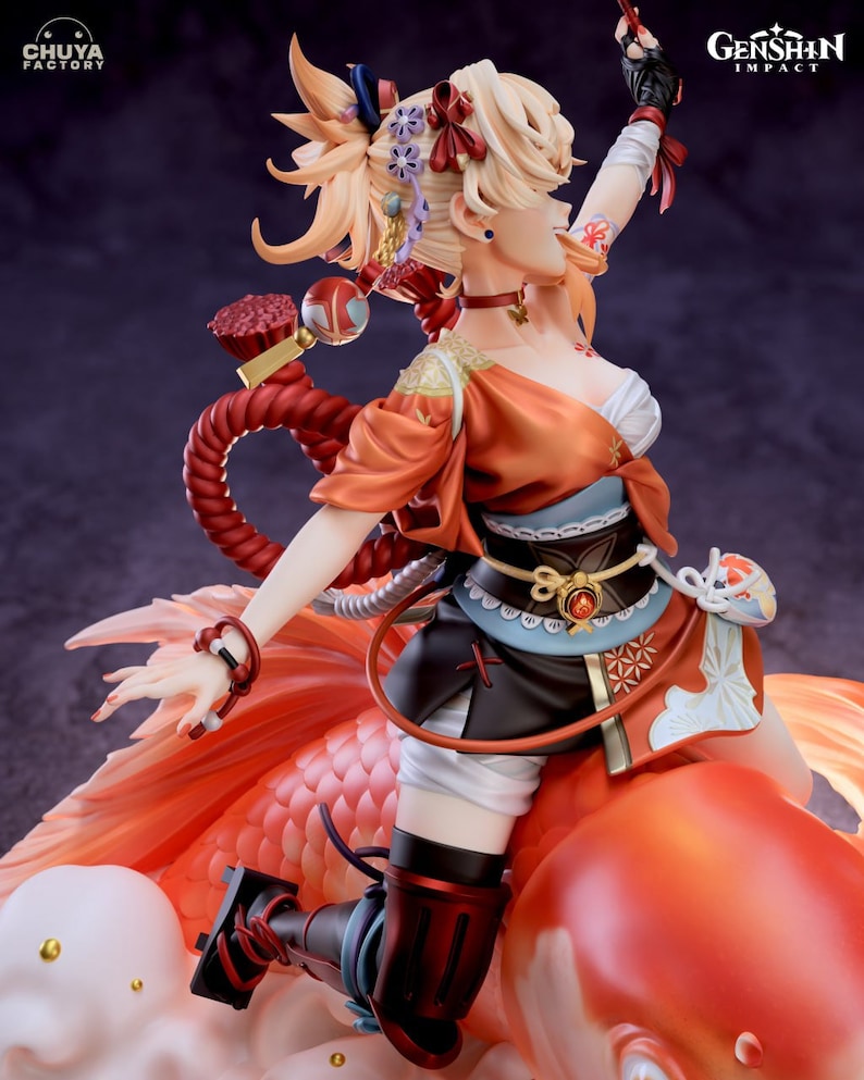 May include: A figurine of a female character from the video game Genshin Impact. She is wearing a red and orange outfit with a white sash and a black belt. She is riding a large, orange goldfish. The figurine is made of high-quality plastic and is very detailed.