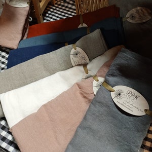 May include: A display of folded linen towels in various colors, including dusty rose, white, and gray. Each towel has a tag with the text "LPK" and a website address. The towels are arranged on a black and white checkered surface.