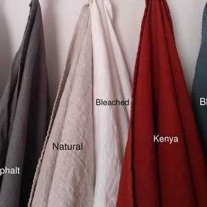 May include: Five linen fabric swatches in various colors hang against a white background. Colors include Insignia Blue, Asphalt, Natural, Bleached, Kenya, and Blue Bayou. Each swatch has a label with its color name.