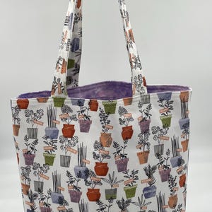 May include: A white tote bag with a purple lining. The bag is decorated with a pattern of potted plants and herbs with handwritten labels.
