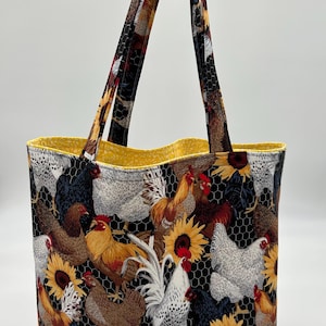 May include: A yellow and black tote bag with a chicken and sunflower print. The bag has two long straps and a yellow lining.