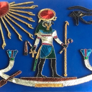 Op de afbeelding: Een blauwe achtergrond met een kleurrijke string art-weergave van een Egyptische god met een zon, een oog en een boot. De god houdt een staf vast en heeft een havikhoofd.