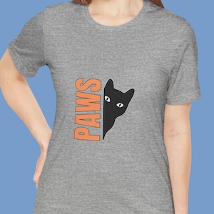 May include: A grey t-shirt featuring the word "PAWS" in orange, alongside a black cat graphic. The cat's head is partially visible. The t-shirt has a crew neck and short sleeves.