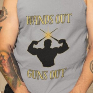 Pode incluir: Uma regata cinza com o texto "Wands Out Guns Out" e uma silhueta de uma figura musculosa segurando duas varinhas cruzadas.