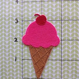 May include: Pink and brown embroidered ice cream cone patch with a red cherry on top.
