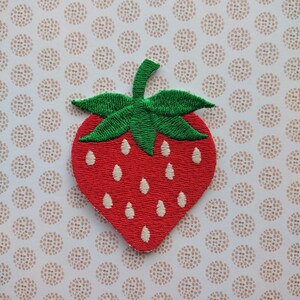 May include: A red and green embroidered strawberry patch. The strawberry is outlined in white and has a green stem and leaves.