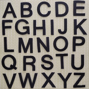 May include: Black felt letters of the alphabet, A through Z, arranged in three rows on a green and white patterned background.