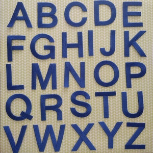 May include: A set of blue felt letters, from A to Z, arranged in alphabetical order. The letters are on a green and white patterned background.