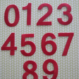 May include: Ten red felt numbers, 0 through 9, arranged in two rows. The numbers are on a light green background with a repeating leaf pattern.