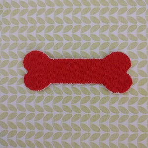 May include: A red felt bone-shaped patch. The patch is on a green and white patterned background.