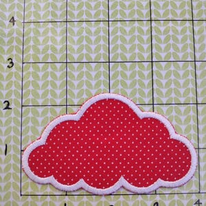 May include: Red fabric cloud with white polka dots and a white stitched border. The cloud is on a green background with a grid.