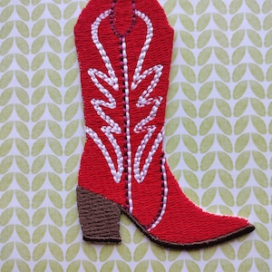 May include: Red cowboy boot with white stitching and a brown heel. The boot is embroidered with a stylized design.