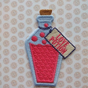 May include: A blue glass bottle with a cork stopper and a pink liquid inside. The bottle has a white tag attached to it that says "Love Potion".