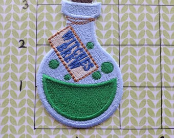 May include: A blue glass bottle with a cork stopper and a green liquid inside. The bottle has a label that says "Witches Brew".