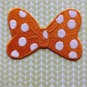 May include: Orange fabric bow with white polka dots. The bow is a flat, iron-on patch.