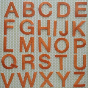 May include: Orange felt letters of the alphabet, A through Z, arranged in rows on a green background.
