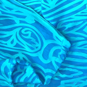 May include: A blue and turquoise patterned fabric with a swirling design. The fabric is folded and has a soft, silky texture.