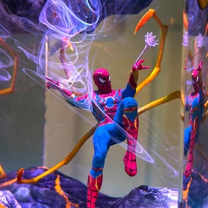 May include: A Spider-Man action figure in a dynamic pose, clad in a red and blue suit, with web-like details. The figure is set against a backdrop of swirling purple and blue energy, with a golden arm extending from the figure.