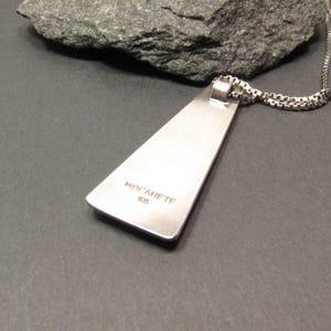 Puede incluir: Collar con colgante de plata con un colgante triangular. El colgante tiene las palabras "MOCARETE 925" grabadas en la parte posterior.
