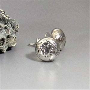 May include: A pair of silver stud earrings with a textured, hammered finish. The earrings are round and have a slightly irregular shape.