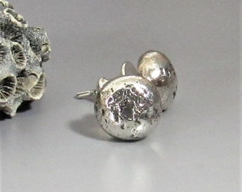 May include: A pair of silver stud earrings with a textured, hammered finish. The earrings are round and have a slightly irregular shape.