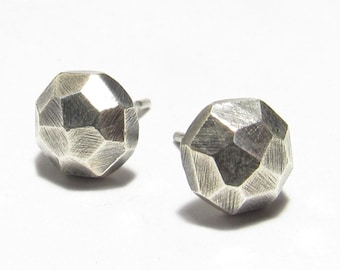 May include: A pair of silver stud earrings. Each earring features a faceted, geometric design, like a small, textured sphere. The earrings are set against a white background, accentuating their metallic sheen.