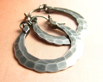 May include: A pair of silver hoop earrings with a hammered texture. The earrings are simple and elegant.