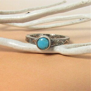 May include: A silver ring with a turquoise stone set in the center. The band of the ring is decorated with a chevron pattern.