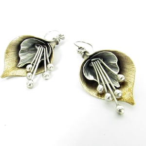 May include: A pair of silver and gold earrings with a flower design. The earrings are made of metal and have a delicate, feminine look.