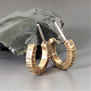 May include: A pair of gold hoop earrings with a textured finish. The earrings are made of brass and have a silver post.