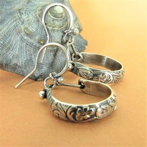 May include: A pair of silver hoop earrings with floral and leaf patterns. The earrings have a hook closure and are displayed against a neutral background. The earrings are small and delicate, suitable for everyday wear.
