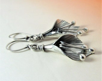 May include: A pair of silver earrings featuring a stylized flower design with textured petals and small silver beads.