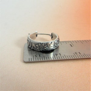 May include: Silver hoop earrings with a floral design. The earrings are approximately 1.5 inches in diameter.