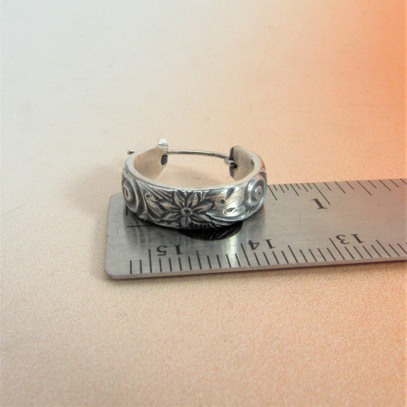 May include: Silver hoop earrings with a floral design. The earrings are approximately 1.5 inches in diameter.