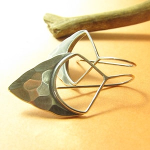 May include: A pair of silver earrings with a geometric design. One earring has a hammered, crescent-shaped design, while the other has a more open, diamond-shaped design.