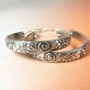 May include: A pair of silver hoop earrings with a floral and swirl design.