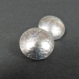 May include: A pair of silver earrings with a textured, hammered finish. The earrings are round and have a slightly domed shape.