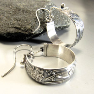 May include: A pair of silver hoop earrings with a floral design. The earrings are made of sterling silver and have a hammered finish.