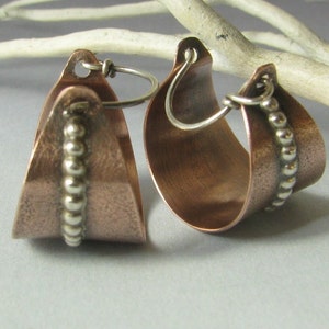 May include: A pair of copper hoop earrings with a hammered finish. One earring has a row of silver beads along the edge.