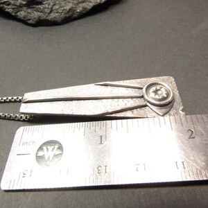 Puede incluir: Un collar con un colgante de plata con un dise&ntilde;o geom&eacute;trico y una estrella en el centro. El colgante mide aproximadamente 3,8 cm de largo.
