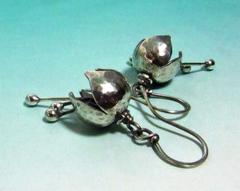 May include: A pair of silver earrings with a hammered metal flower design. The earrings have a dangling drop shape with a small ball at the end of the wire.