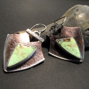 Copper and sterling silver frame unusual lemon chrysoprase cabochons for a uniquely different pair of earrings. Eye catching and soulful the distressed copper, patterned sterling silver wire and the coppery matrix in the yellow green chrysoprase all play together for a  pair of one of a kind earrings. These mixed metal earrings will allow you to mix with other copper or silver jewelry.

Earrings measure apx 1 inch wide x 2 inch long.
Each earring 5.25 grams each.