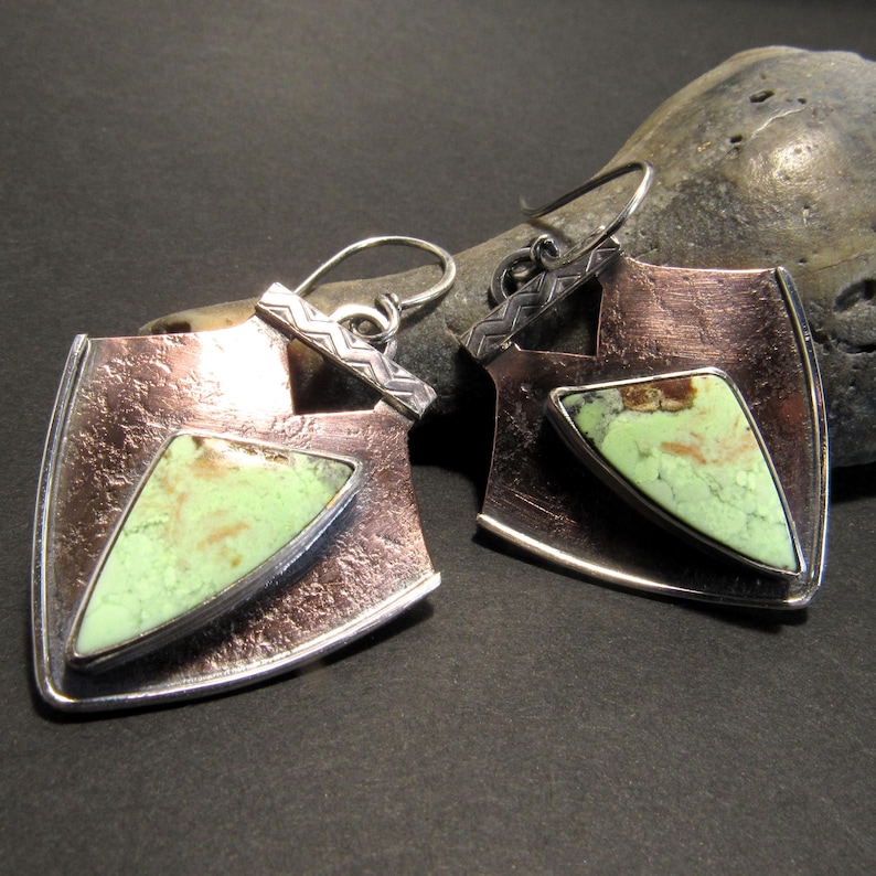 Copper and sterling silver frame unusual lemon chrysoprase cabochons for a uniquely different pair of earrings. Eye catching and soulful the distressed copper, patterned sterling silver wire and the coppery matrix in the yellow green chrysoprase all play together for a  pair of one of a kind earrings. These mixed metal earrings will allow you to mix with other copper or silver jewelry.

Earrings measure apx 1 inch wide x 2 inch long.
Each earring 5.25 grams each.