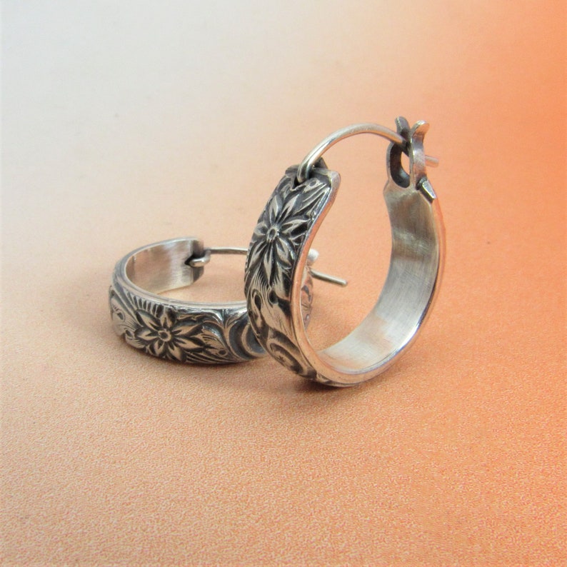 May include: A pair of silver hoop earrings with a floral design. The earrings are made of metal and have a polished finish.