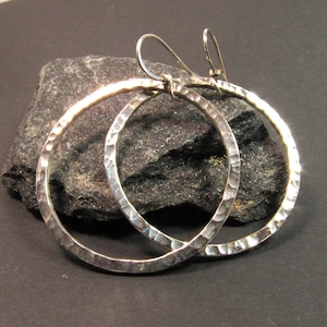 May include: A pair of silver hoop earrings with a hammered texture. The earrings are large and have a simple, elegant design.