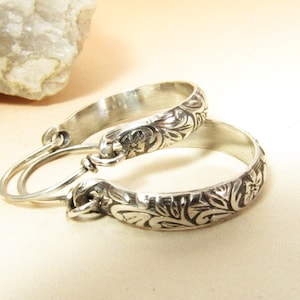 May include: A pair of silver hoop earrings with a floral design. The earrings are made of sterling silver and have a polished finish.