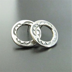 May include: A pair of silver earrings with a geometric design. The earrings are round and have a textured surface.
